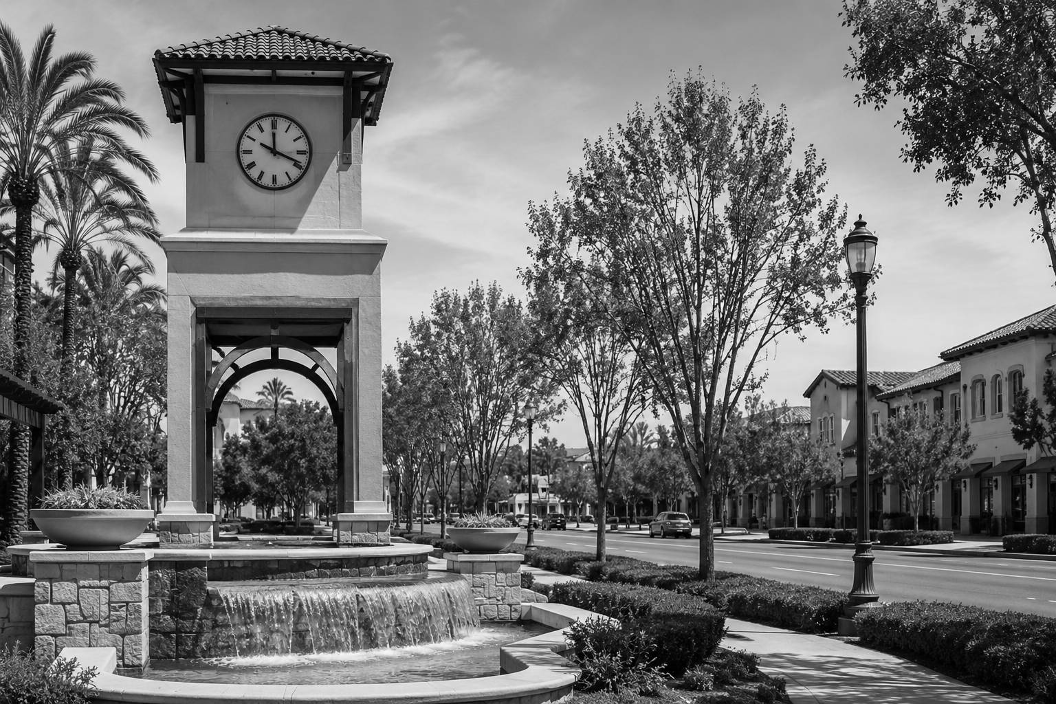 Black and white view of a tree-lined Tustin, California streetscape with a Spanish-style clock tower, fountain, palm trees, and surrounding buildings.